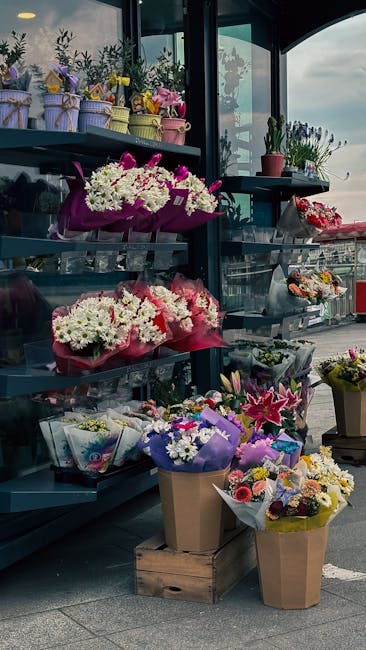 An exterior display of fresh floral arrangements at floristcolindale.co.uk, featuring a variety of bouquets including white chrysanthemums accented with pink wrapping and purple ribbons, arranged on m