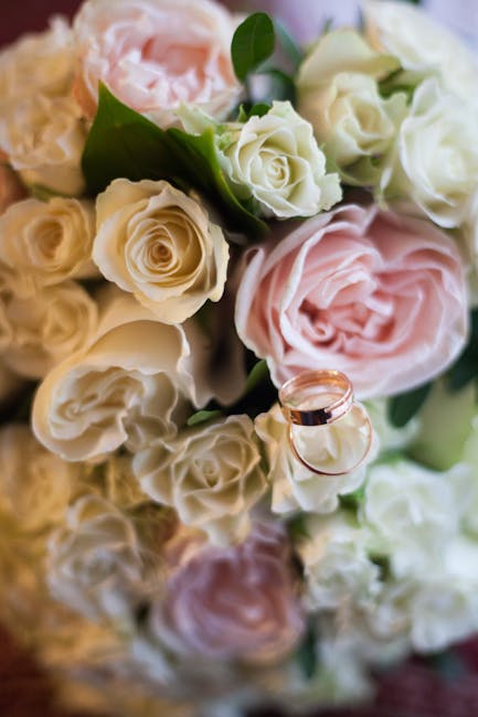 A close-up view of a bouquet arrangement featuring creamy white and soft pink roses with delicate petals and lush green leaves, arranged in a natural, slightly loose style. Some roses are in full bloo